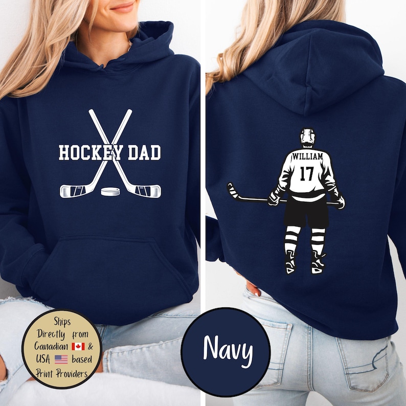 Puede incluir: Sudadera con capucha azul marino con gr&aacute;ficos blancos. La parte delantera presenta "HOCKEY DAD" con palos de hockey cruzados y un disco. La parte trasera muestra un jugador de hockey con el nombre "WILLIAM" y el n&uacute;mero "17".