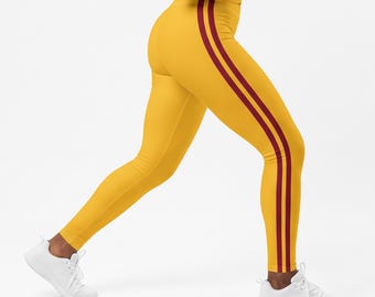 May include: A mustard yellow sleeveless tank top and matching leggings set. The leggings feature two vertical dark red stripes running down the outer side of each leg. The outfit is paired with white athletic sneakers.