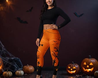 May include: A black long-sleeved crop top paired with orange leggings featuring a Halloween-themed print. The leggings display a black silhouette pattern of bare trees, a graveyard, a witch on a broomstick, and a reaching hand against an orange background.