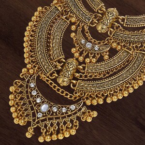 Make a bold impact with this antique gold bib necklace, featuring intricate engravings and resin stones designed for high-drama festival looks. Whether you are channeling a desert queen or elevating a bohemian outfit, this layered piece sits perfectly against the collarbone to command attention. Inspired by traditional nomadic adornments, this necklace uses weightier textures and a multi-tiered design to create movement and sound as you move.