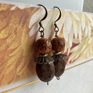 May include: A pair of brown and orange earrings with a decorative metal accent. The earrings are made of wood and have a natural, rustic look.