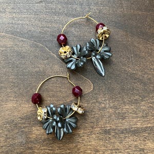 May include: A pair of gold hoop earrings with black flower-shaped charms and burgundy beads.