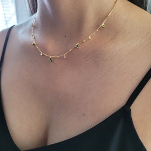 Könnte beinhalten: Eine goldene Kettenkette mit kleinen grünen und klaren Steinen, die daran hängen.
