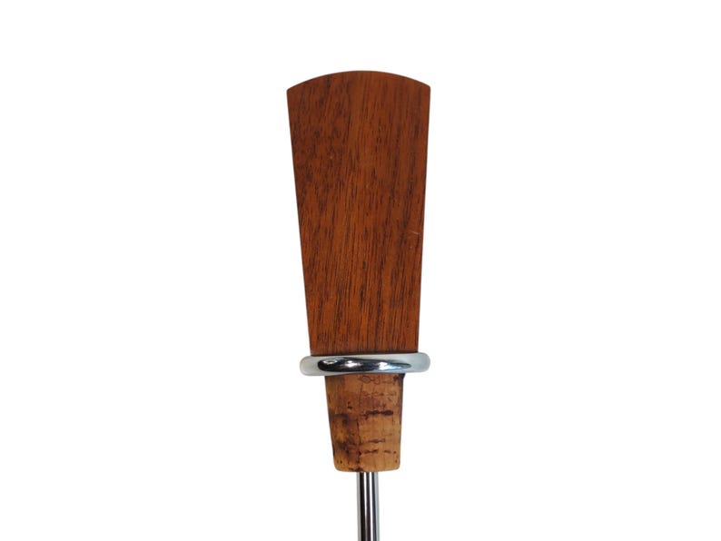 May include: A bottle stopper featuring a tapered, reddish-brown wooden handle with a visible grain pattern. A smooth, silver-toned metal ring separates the wooden top from the natural, light-brown cork base, which is attached to a thin metal stem.