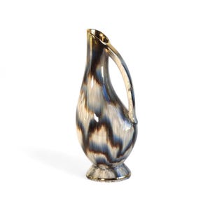 May include: A ceramic vase with a blue, brown, and white abstract pattern. The vase has a gold rim and a curved handle.