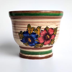 May include: A ceramic planter with a brown, cream and green striped design. The planter has a floral design with blue and pink flowers.