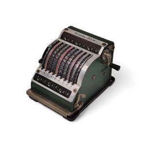 Op de afbeelding: Een antieke groene en zilveren mechanische rekenmachine met meerdere nummerknoppen. De rekenmachine heeft een zwarte hendel en de tekst "Resulta-BSO" is zichtbaar aan de bovenkant. De rekenmachine staat op een zwarte basis.