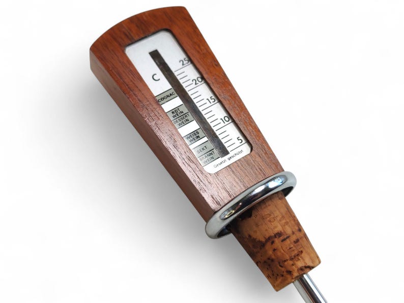 May include: A wooden wine thermometer with a silver metal ring and a cork base. The white display features a temperature scale in Celsius and labels for various beverages including Cognac, Rot Wein, Dessert Wein, Weiss Wein, Sekt, and Brannt Wein.