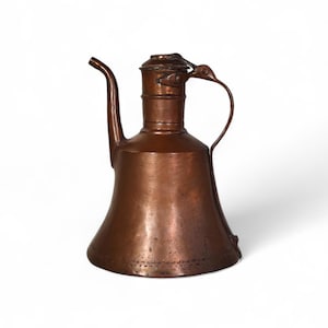 May include: A copper teapot with a wide, bell-shaped body and a long, curved spout. The teapot has a handle with a decorative bird design.