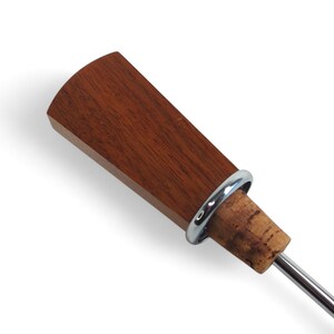 May include: A bottle stopper featuring a flat, fan-shaped top made of reddish-brown wood. A polished silver-colored metal ring separates the wooden top from a natural tan cork base, which is attached to a thin, straight silver-colored metal rod.