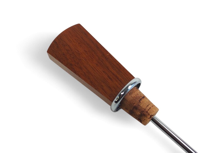 May include: A bottle stopper featuring a flat, fan-shaped top made of reddish-brown wood. A polished silver-colored metal ring separates the wooden top from a natural tan cork base, which is attached to a thin, straight silver-colored metal rod.