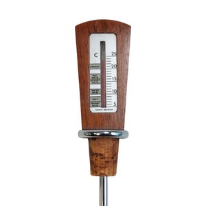 May include: A wine thermometer with a wooden handle featuring a vertical scale from 5 to 25 degrees Celsius. The display includes labels for Cognac, Rotwein, Dessertwein, Weisswein, and Sekt. A silver metal ring separates the handle from a cork stopper.