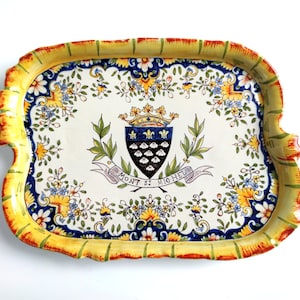 May include: A yellow and blue ceramic tray with a floral design and a coat of arms featuring a crown and the text "MONT ST MICHEL".
