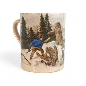 May include: A ceramic mug with a tan handle and a detailed illustration depicting a bear attack scene in a snowy forest. The artwork features figures in blue and brown clothing, with trees in the background.