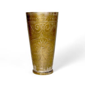 Peut inclure: Une grande tasse en laiton antique avec des motifs floraux et tourbillonnants complexes gravés sur sa surface. La tasse a une forme légèrement évasée et un bord décoratif, mettant en valeur une esthétique vintage.