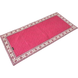 May include: A rectangular, quilted rug in a vibrant fuchsia color. The rug features a detailed border with a repeating pattern of floral and geometric elements in cream, brown, and burgundy. The rug's dimensions are not visible.