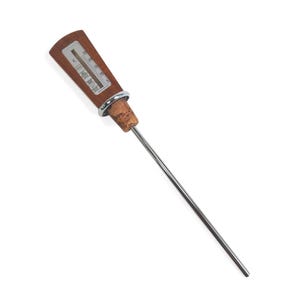 May include: A kitchen thermometer with a long, thin stainless steel probe, a cork stopper base, a silver-colored metal ring, and a rectangular wooden handle featuring a vertical temperature scale marked in degrees Celsius and Fahrenheit.