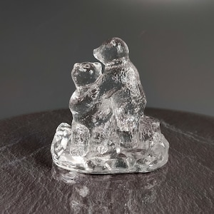 May include: A glass figurine of two bears, one sitting on top of the other, with a textured base. The bears are clear glass and appear to be hugging.