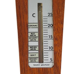 May include: A wooden wine thermometer with a vertical scale in Celsius ranging from 5 to 25 degrees. The white display features black text labels for COGNAC, ROT WEIN, DESSERT WEIN, WEISS WEIN, SEKT, and BRANNT WEIN, with the text Gesetzi. gesch&uuml;tzt at the bottom.