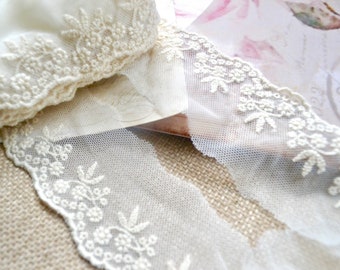 May include: Close-up of ivory lace trim with floral embroidery. The delicate lace is layered, showcasing intricate details and textures. The trim is likely used for sewing, crafting, or adding a vintage touch to various projects.