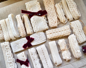May include: An assortment of cream-colored lace ribbons in various widths and patterns, including floral and geometric designs. Some ribbons are tied with burgundy velvet bows. A spool of twine and a small wooden spool with a pin are also present.