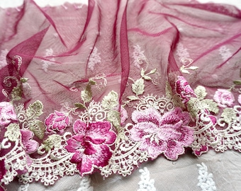 May include: A sheer burgundy mesh fabric featuring an intricate embroidered border. The trim displays vibrant pink floral blossoms with sage green leaves and cream-colored scalloped lace edges, creating a detailed botanical pattern across the fabric.