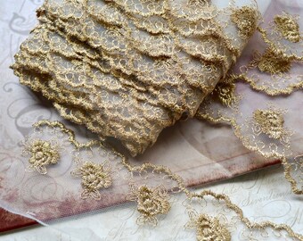 May include: A roll of gold-colored lace trim with a floral design. The lace is layered and has a scalloped edge. The trim is on a white mesh fabric. The background has a vintage paper design.