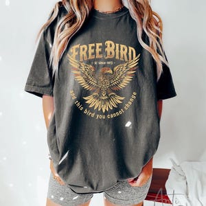 May include: A dark gray t-shirt with a vintage-style graphic of an eagle with the text "Free Bird - since 1973 - and this bird you cannot change".