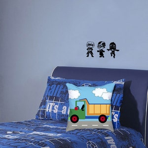 May include: A blue bed with a blue and white patterned bedspread and a pillow with a truck graphic. The wall behind the bed has three black silhouettes of people.