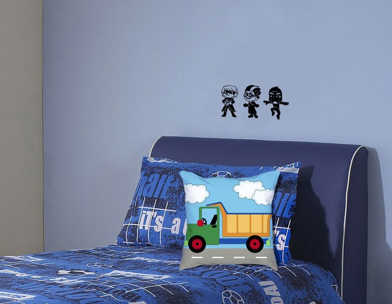 May include: A blue bed with a blue and white patterned bedspread and a pillow with a truck graphic. The wall behind the bed has three black silhouettes of people.