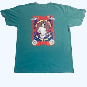 May include: Teal blue t-shirt with a graphic print of a man playing a guitar. The graphic has the text "Let Where Be Songs" and "To Phil The Air".