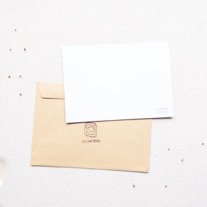 May include: A brown envelope with a white card on top. The envelope has a small, circular logo with a swirl design and the text "sue van den bergh" printed on it.