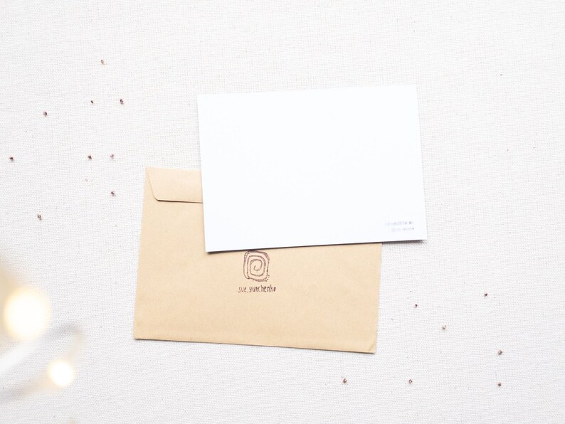 May include: A brown envelope with a white card on top. The envelope has a small, circular logo with a swirl design and the text "sue van den bergh" printed on it.