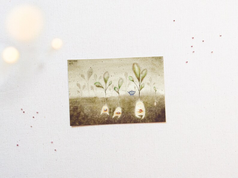 May include: A watercolour painting of five small, green plants with white roots and faces. The plants are growing in brown soil. A small blue teapot sits between two of the plants.