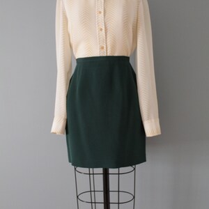 May include: A white button-down shirt with a chevron pattern and a dark green skirt. The shirt has long sleeves and a collared neckline. The skirt is knee-length and has a straight silhouette.