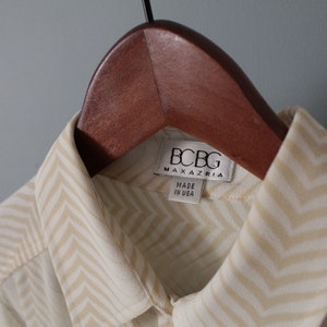 May include: A white and beige chevron patterned shirt with a BCBG Max Azria label. The label says "Made in USA".