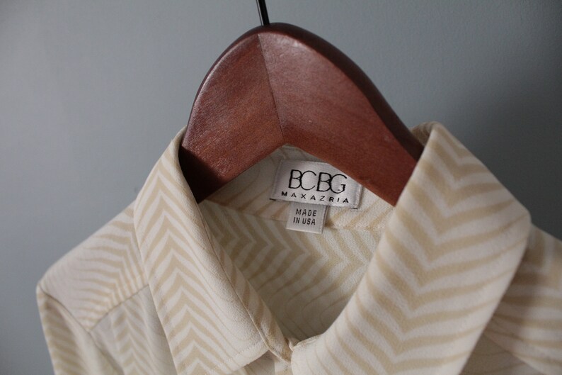 May include: A white and beige chevron patterned shirt with a BCBG Max Azria label. The label says "Made in USA".