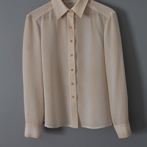 May include: A white long-sleeved button-down shirt with a yellow chevron pattern. The shirt has a collar and is hanging on a wooden hanger.