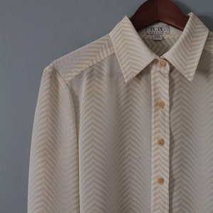 May include: A white long-sleeved button-down shirt with a chevron pattern. The shirt has a collar and is made of a silky fabric. The brand label reads "BCBG Max Azria" and "Made in USA".