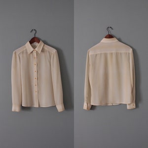 May include: A white long-sleeved blouse with a chevron pattern in a lighter shade of yellow. The blouse has a button-up front and a collared neckline.
