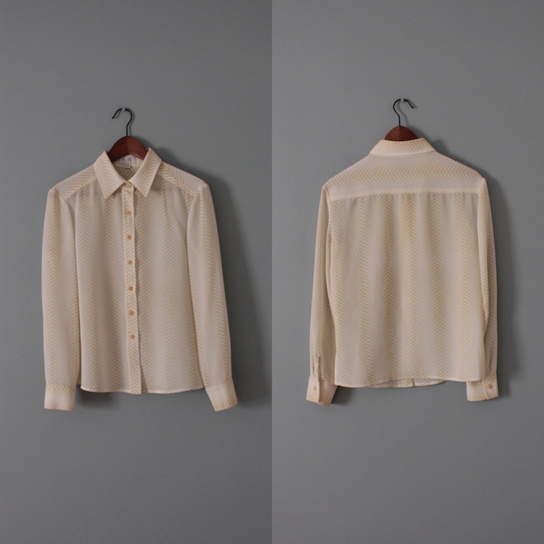May include: A white long-sleeved blouse with a chevron pattern in a lighter shade of yellow. The blouse has a button-up front and a collared neckline.