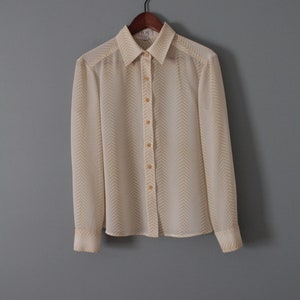 May include: A white long-sleeved button-down shirt with a yellow chevron pattern.