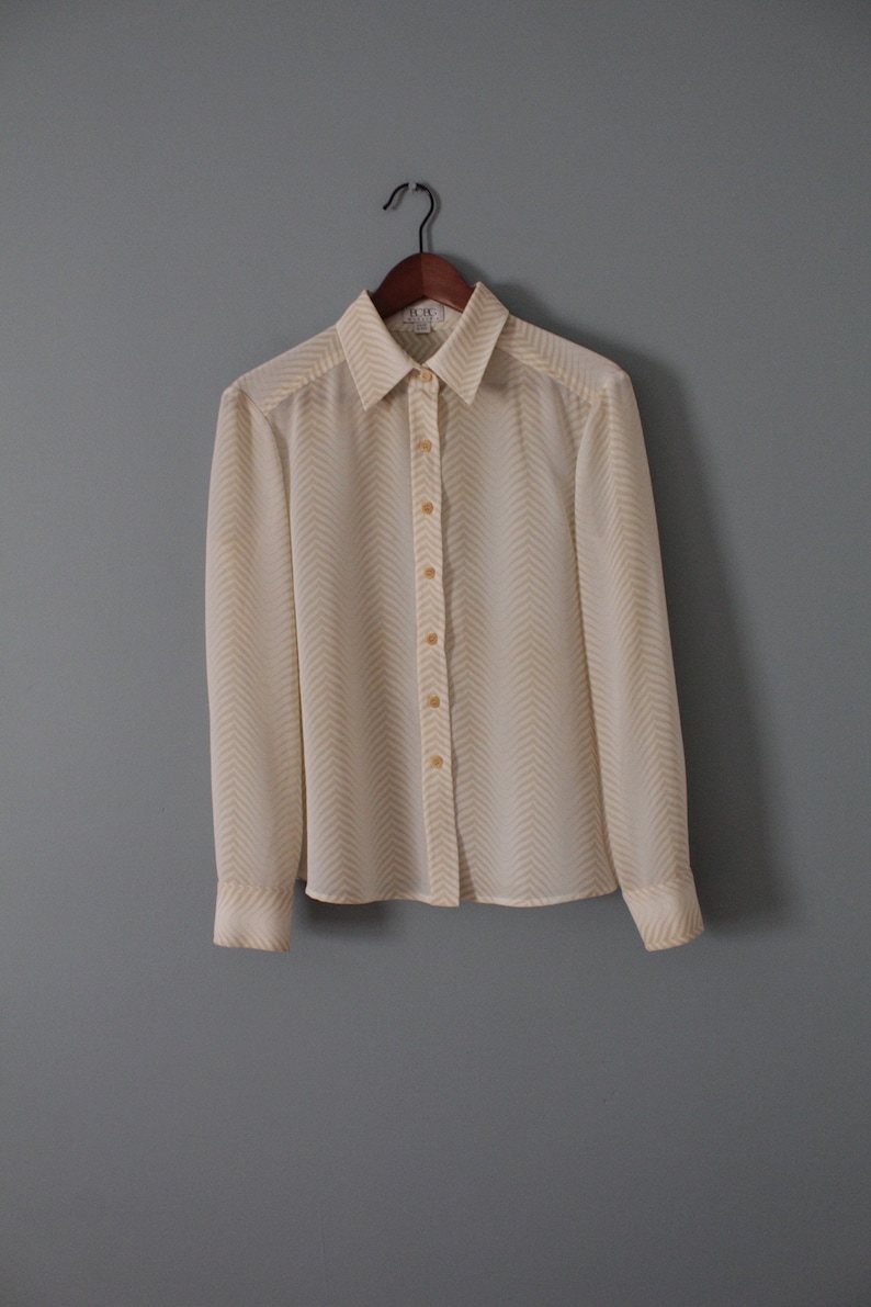 May include: A white long-sleeved button-down shirt with a yellow chevron pattern.