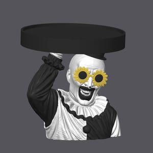 May include: A black and white clown bust featuring a wide grin and yellow sunflower-shaped sunglasses. The clown wears a ruffled collar and holds a flat, circular black tray above its head with one raised arm, showcasing a detailed monochromatic design.