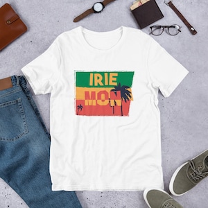 May include: White t-shirt with a graphic design of a red, yellow, and green flag with palm trees and the text "IRIE MON".