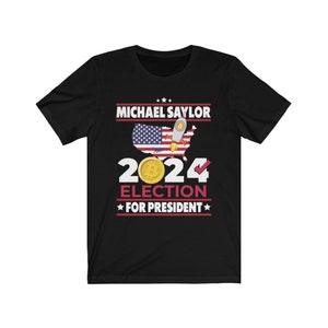 May include: Black t-shirt featuring a graphic of a US map with an American flag, a Bitcoin logo, and a rocket. The text "MICHAEL SAYLOR 2024 ELECTION FOR PRESIDENT" is printed on the shirt.