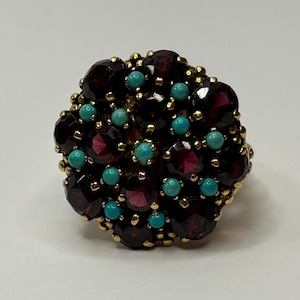 Puede incluir: Un anillo de oro con un grupo de piedras de granate rojo y turquesa.