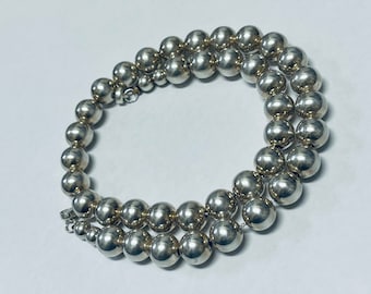May include: A silver necklace with round beads. The necklace is made of many small, round beads that are all the same size. The beads are silver in colour and have a shiny finish.
