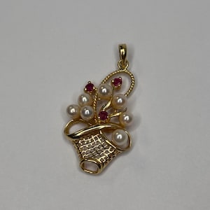 May include: A gold pendant featuring a basket design filled with pearls and red gemstones. The pendant has a delicate, openwork basket shape with a bail for a chain. The pearls and gemstones are arranged to resemble flowers.