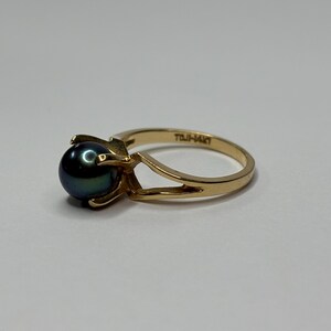 Puede incluir: Un anillo de oro con una perla oscura e iridiscente. El anillo tiene un dise&ntilde;o de ca&ntilde;a dividida y un engaste de cuatro puntas. La banda est&aacute; estampada con "TOJI-14KT".